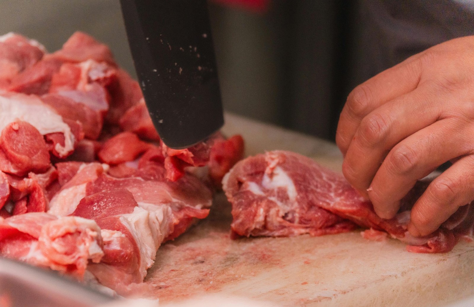Close-up view of hands cutting raw meat with a knife on a chopping board, ideal for culinary or food safety topics.